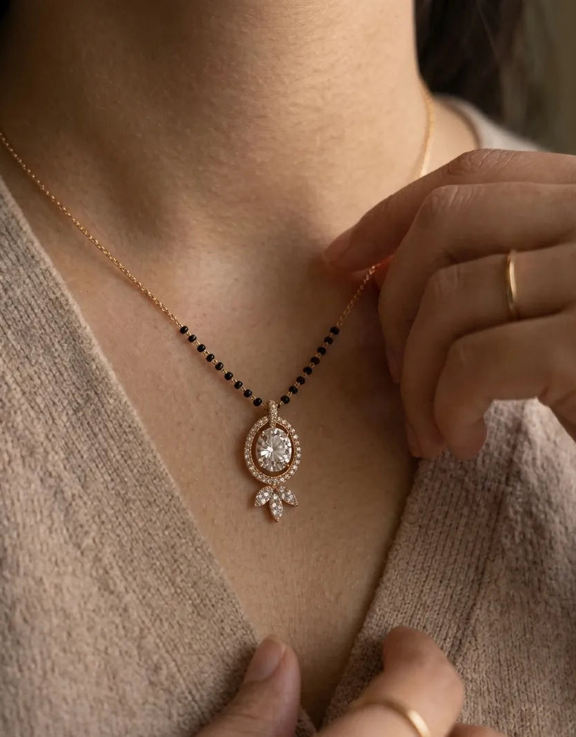 Necklace with a pendant being adjusted on a person wearing a beige sweater.